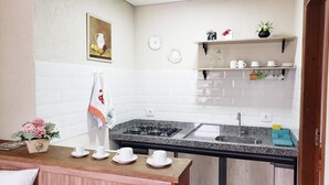 A kitchen with white tiled walls, a gas stove, a sink, and a countertop with cups and a vase of flowers. - Suites Bela João e Maria (Campos do Jordão)