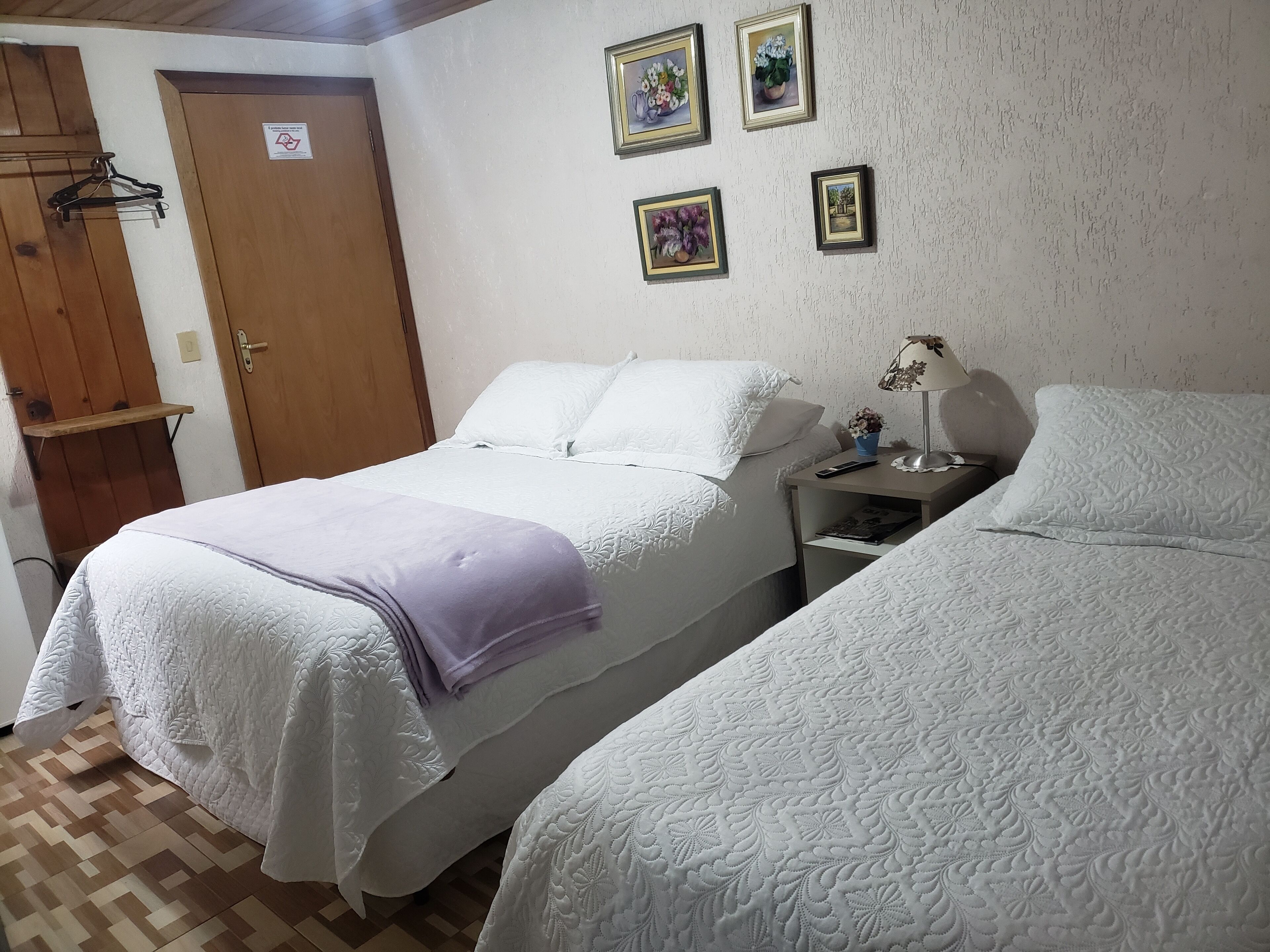 Una habitación con dos camas, una puerta de madera y una pared con tres cuadros enmarcados.