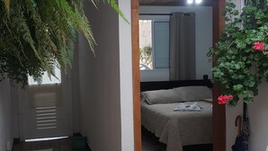 A cozy room with a bed, a wooden table, and a hanging plant. - Suites Bela João e Maria (Campos do Jordão)