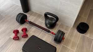 Un espace de musculation à domicile équipé d’une barre d’haltères, de kettlebells, d’une plateforme de step et d’un tapis de yoga.