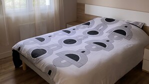 Une chambre à coucher avec un lit, un plancher en bois, une fenêtre avec des rideaux légers et un luminaire suspendu.