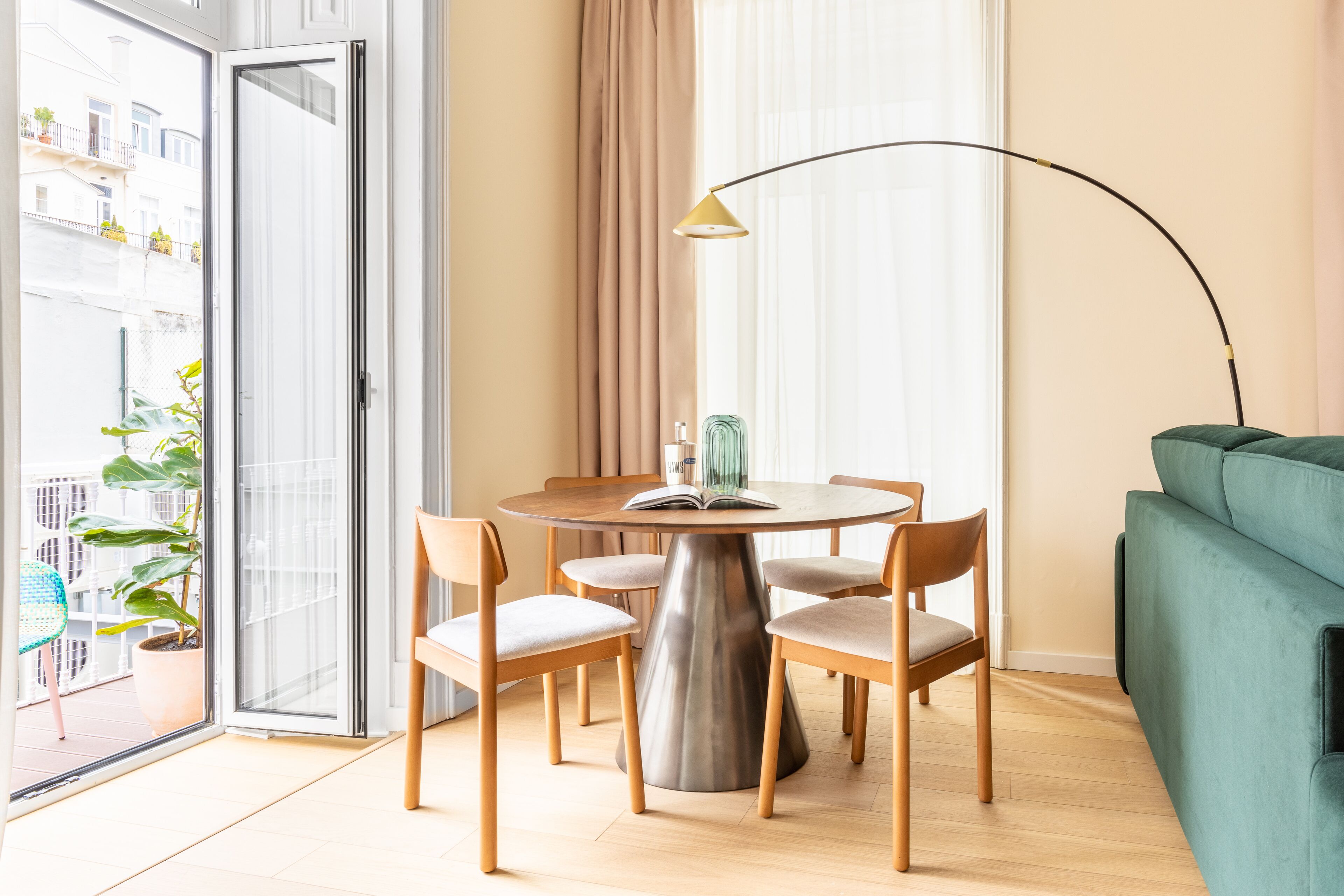 A modern living room with a round dining table, four chairs, a green sofa, and a floor lamp.