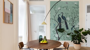 Un comedor con una mesa redonda de madera, cuatro sillas, un florero con limones y un mural grande de pájaros y flores.