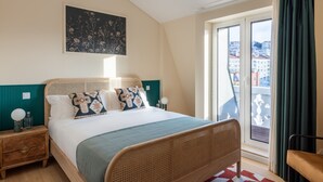 Un dormitorio con cama, mesita de noche, ventana con cortinas y vista a edificios.