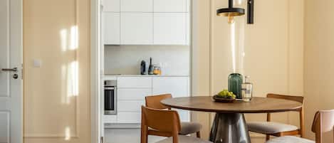 Una cocina moderna con armarios blancos, un horno de acero inoxidable y un comedor con una mesa redonda y cuatro sillas de madera.