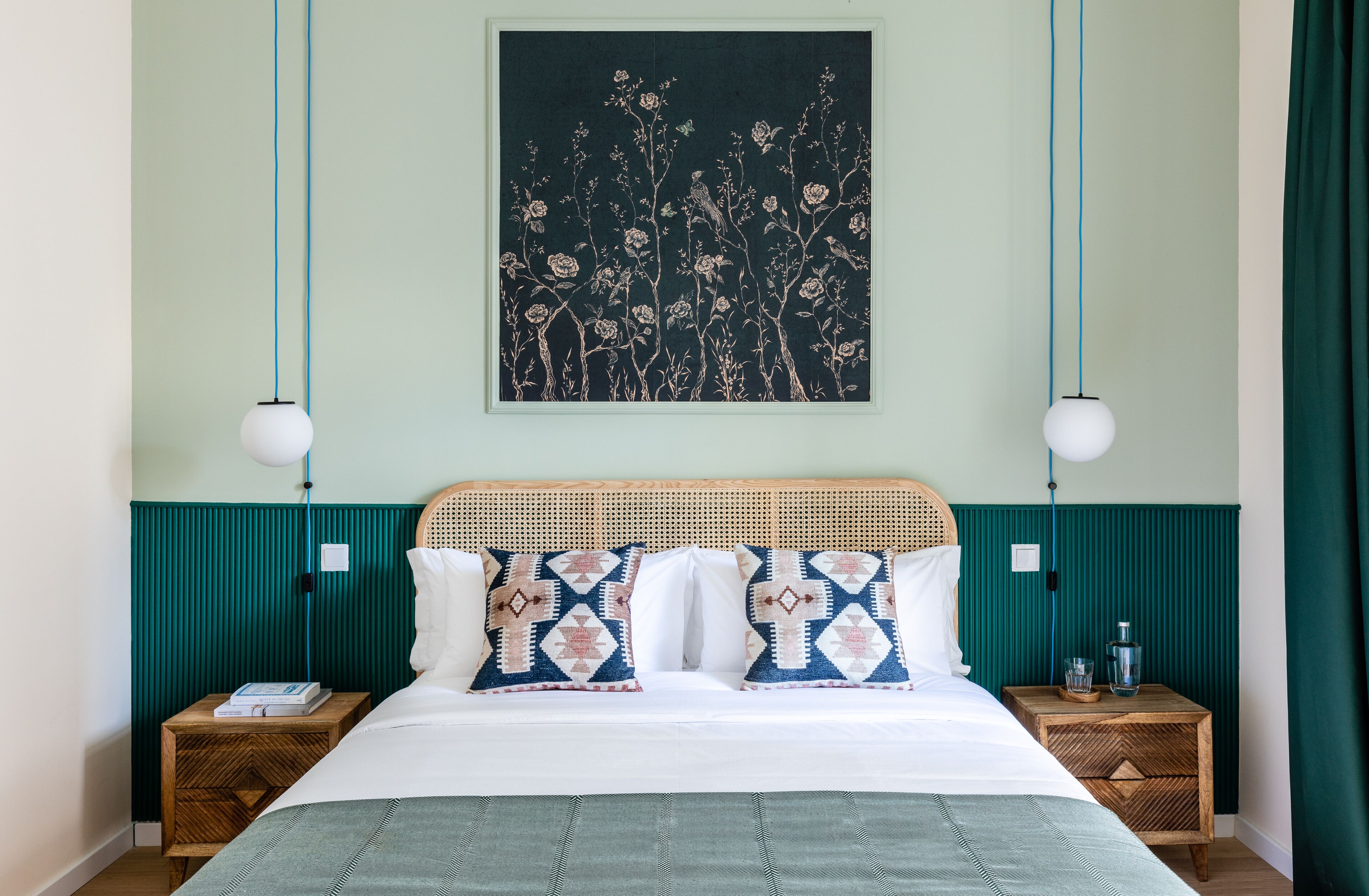 A neatly arranged bedroom with a bed, two bedside tables, a wall-mounted artwork, and a hanging light fixture.