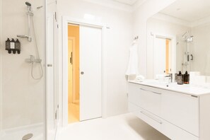 A modern bathroom with a glass-enclosed shower, a white vanity with a mirror, and a door leading to another room. - Haws Lisboa (Lisbon)