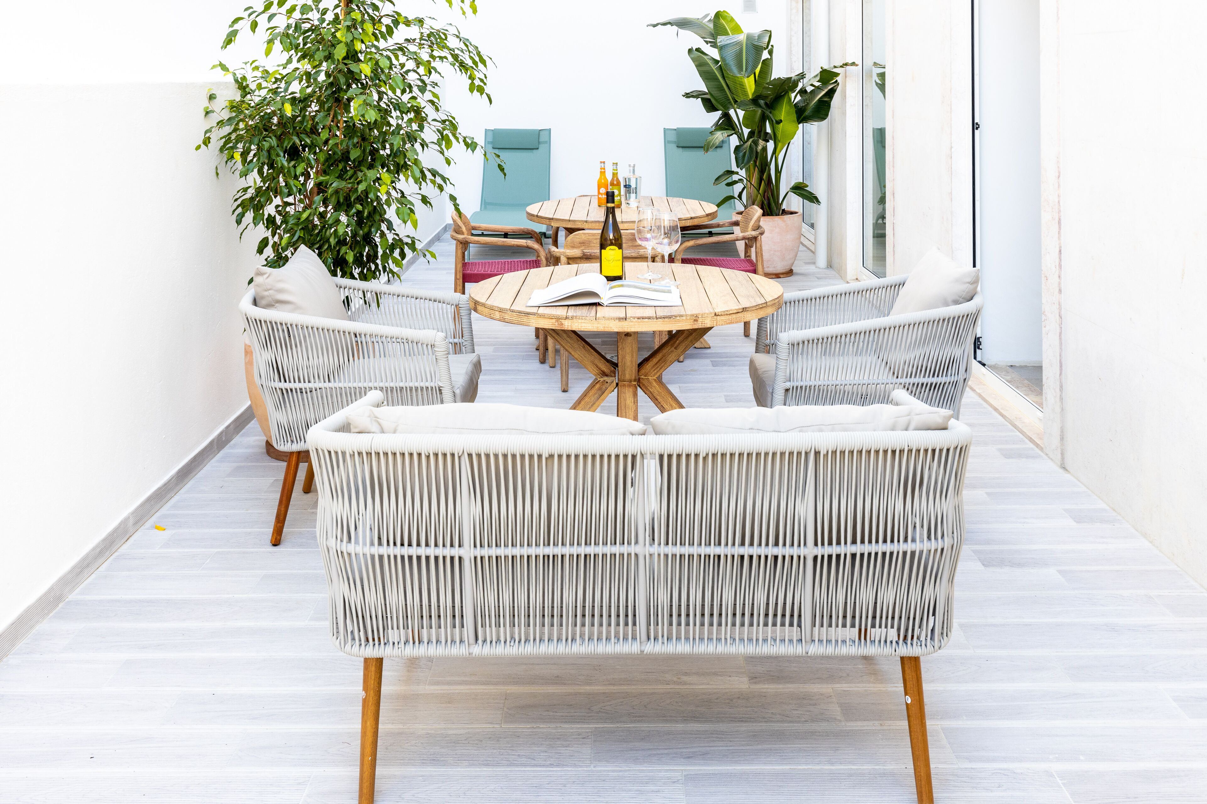 A round wooden table with wicker chairs, a bottle, and a glass on it.