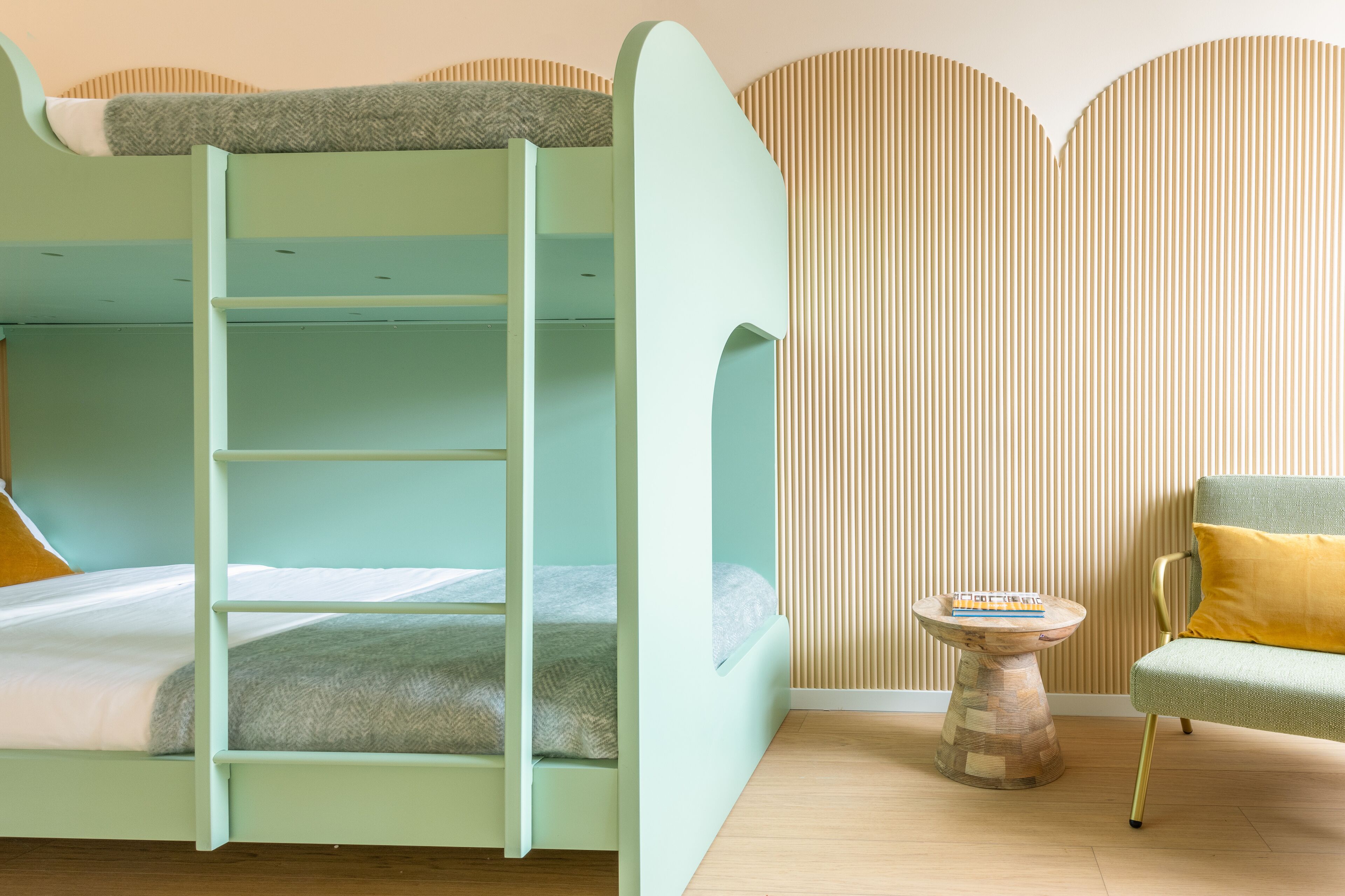 Uma cama beliche com escada, uma mesinha redonda com um livro e um sofá com almofada.