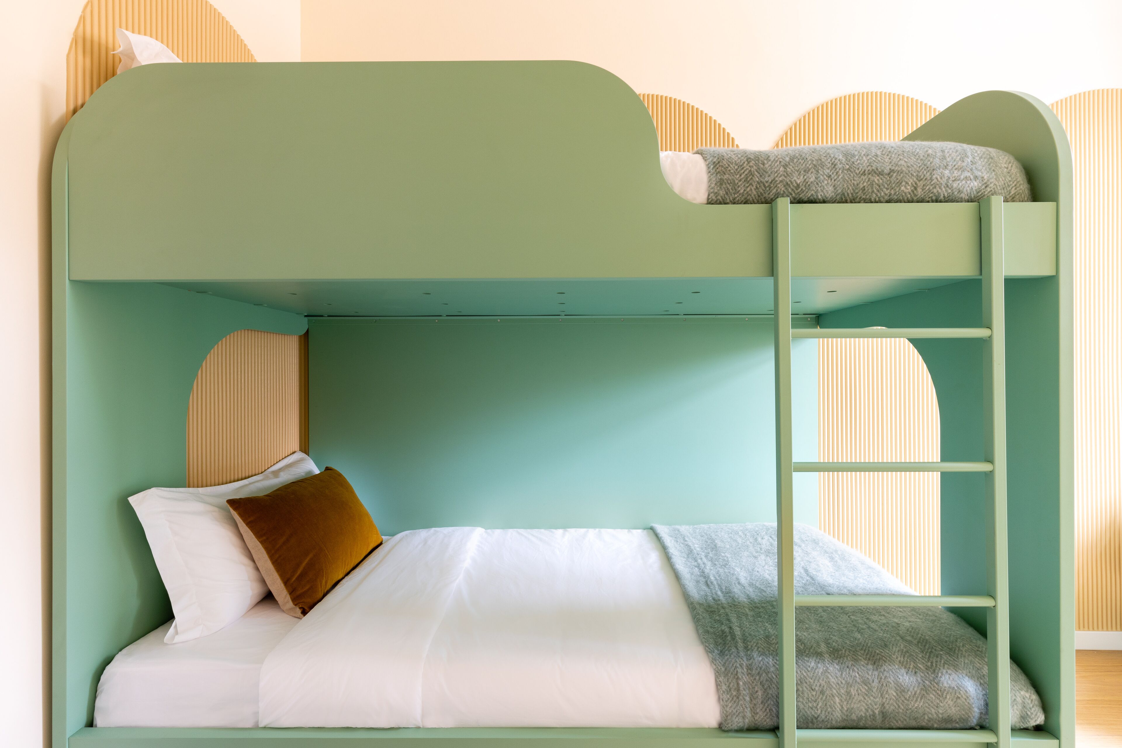 A bunk bed with a ladder, white bedding, and a brown pillow.