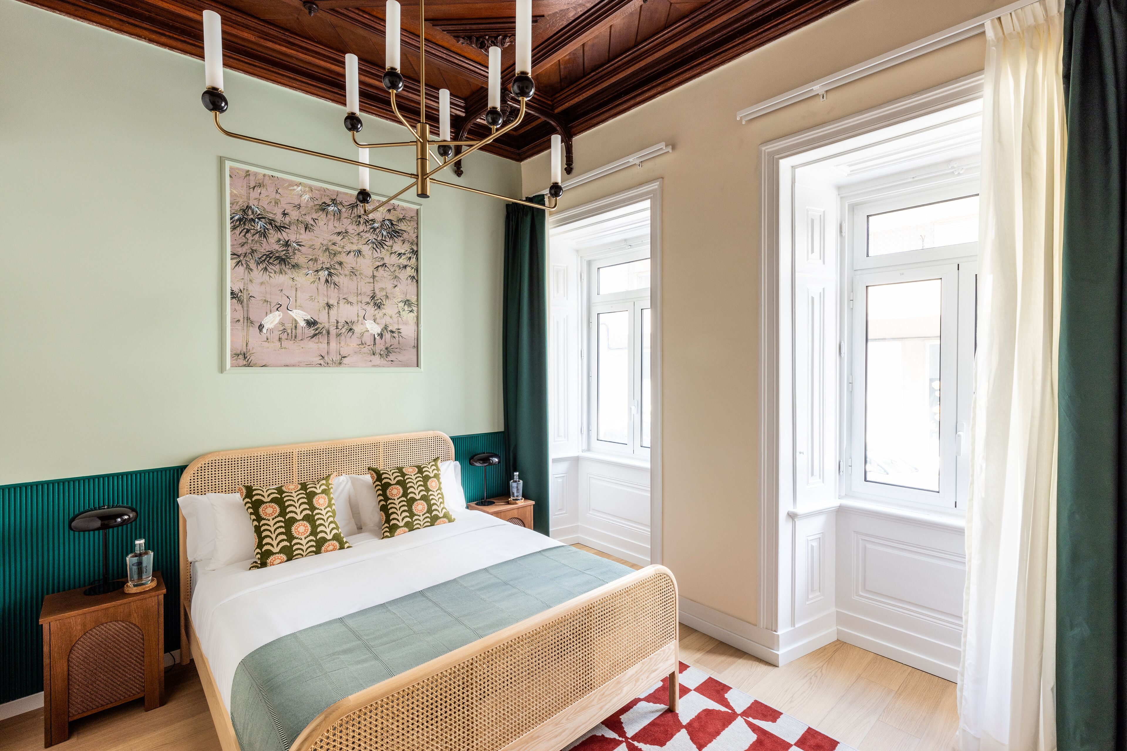 A bedroom with a bed, bedside tables, a hanging light fixture, and a window with curtains.