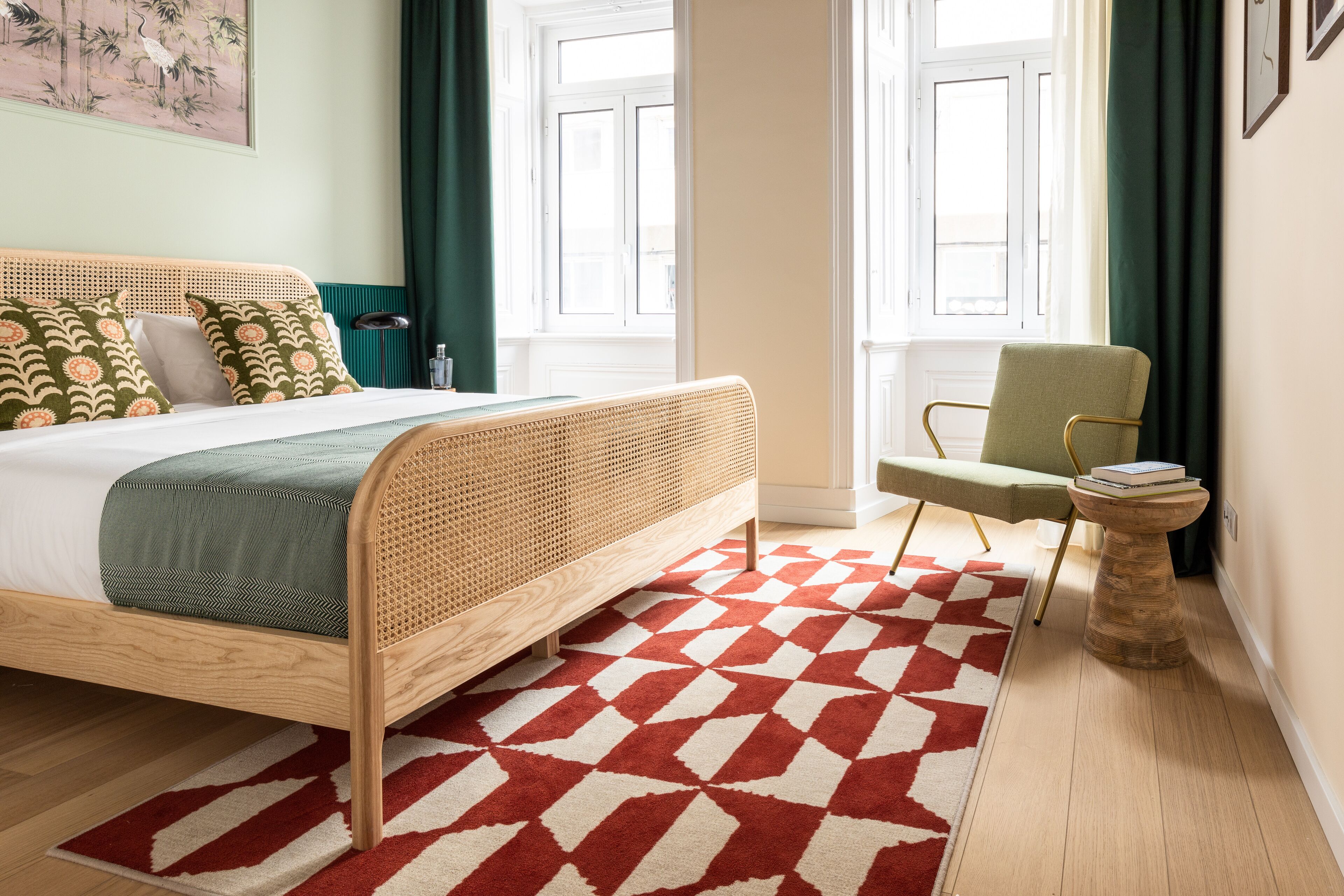 Ein Zimmer mit einem Bett, einem Sessel, einem kleinen Tisch und einem Fenster mit Vorhängen.