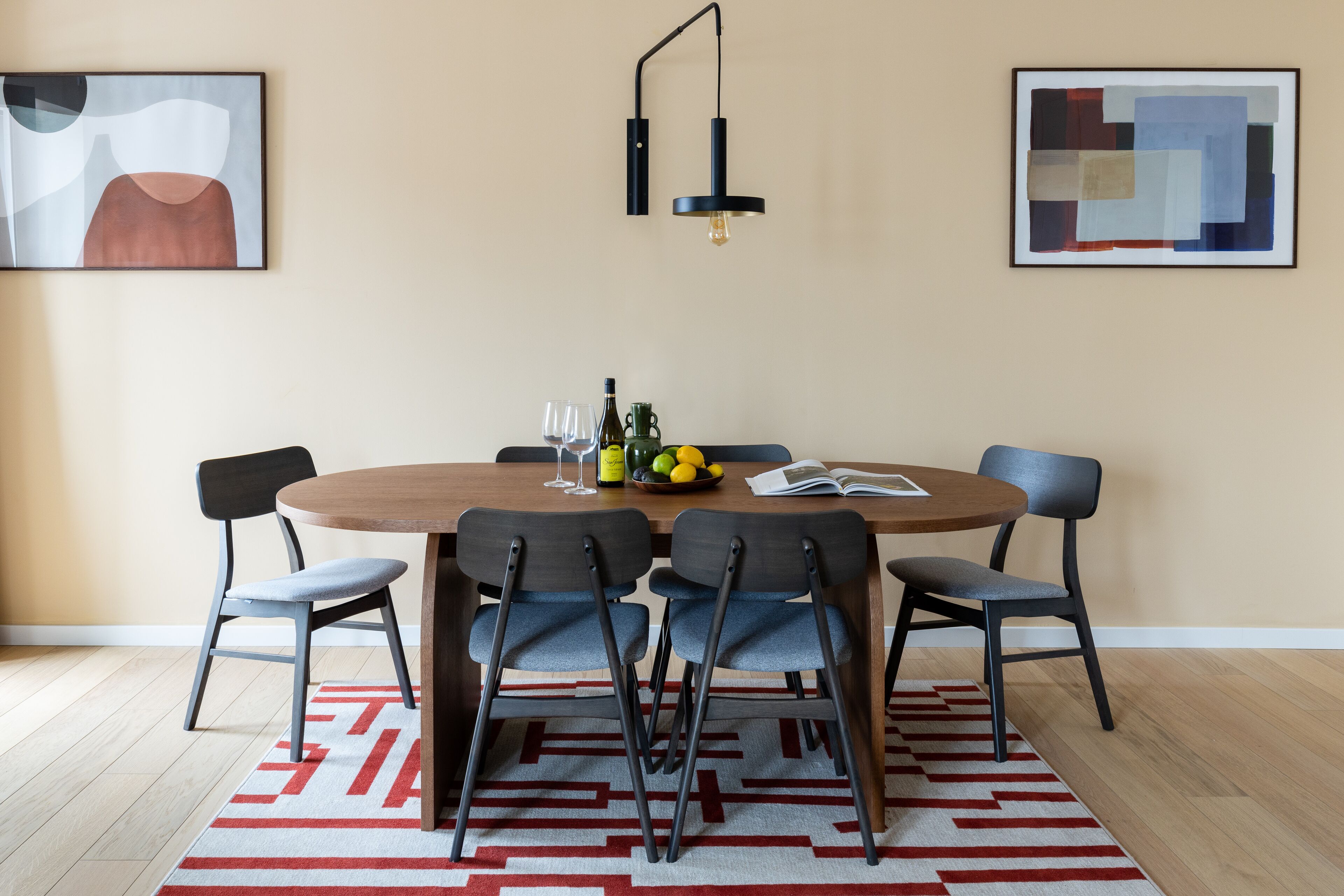 Uma sala de jantar com uma mesa redonda, seis cadeiras, duas luminárias fixadas na parede e arte abstrata nas paredes.