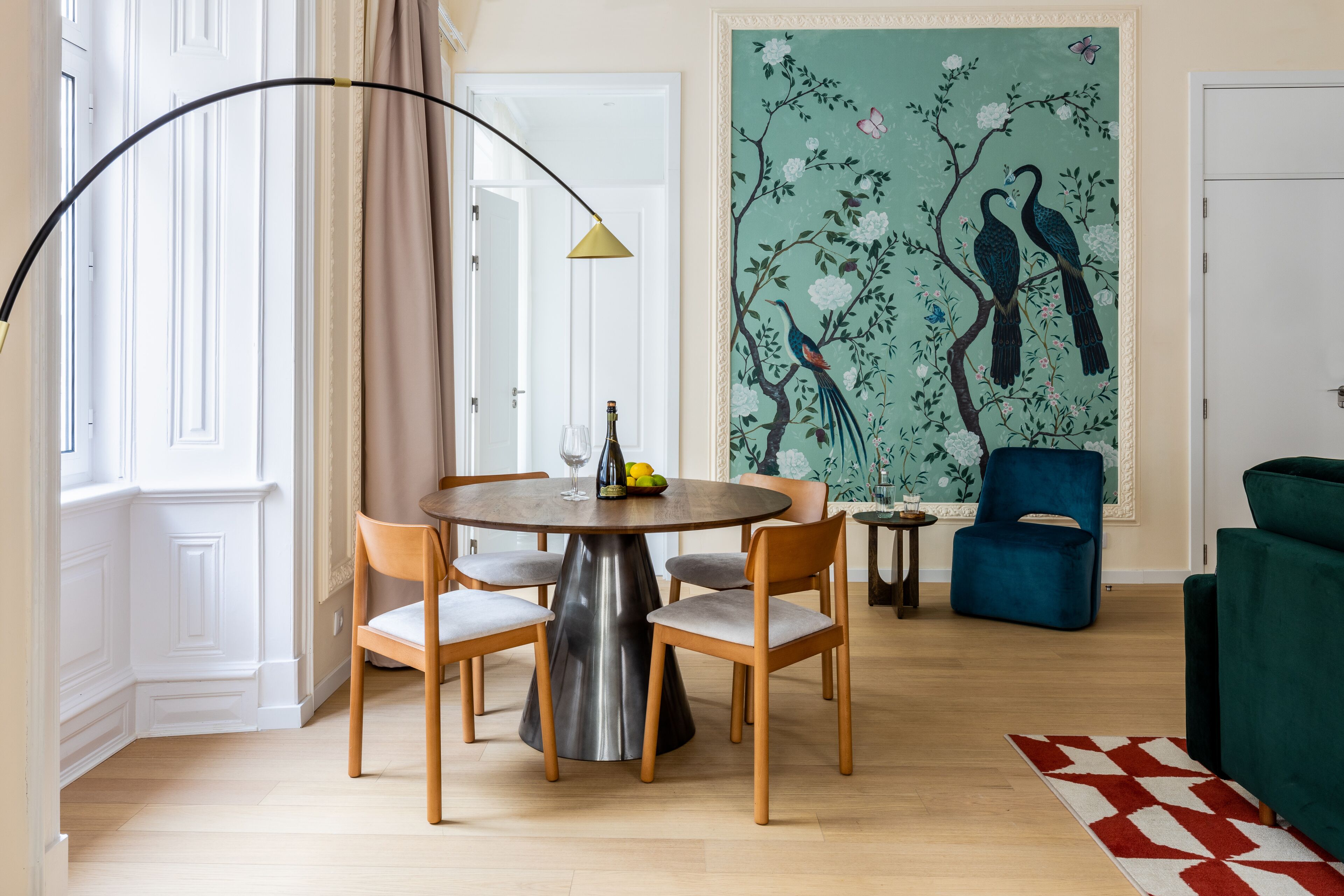 A dining area with a round table, chairs, a lamp, and a painting of birds on the wall.