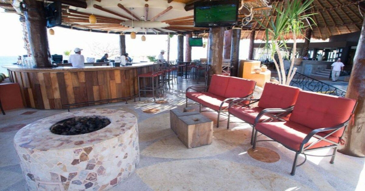 Un área de bar al aire libre con un hogar de piedra, asientos acolchados rojos y una barra de madera.