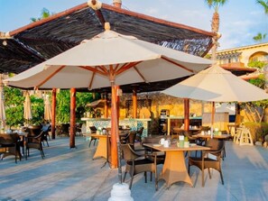 An outdoor dining area with tables and chairs, umbrellas, and a bar area.