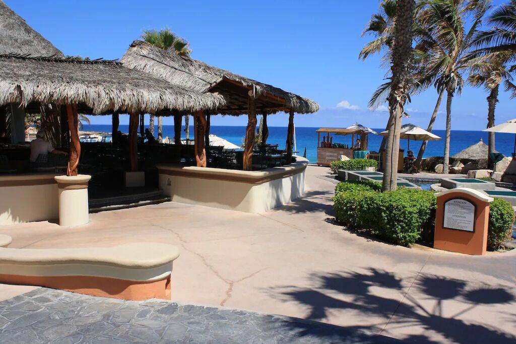 A resort area with thatched-roof structures, outdoor seating, a pool, and palm trees.