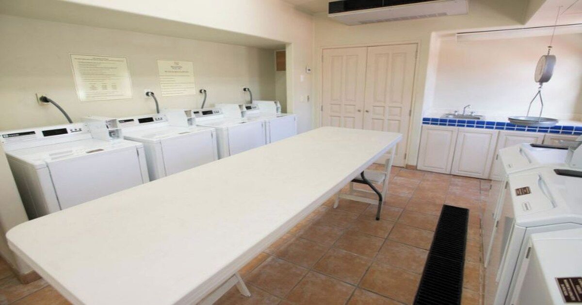 Un lavadero con varias lavadoras y secadoras, una mesa larga y una zona de cocina con un lavaplatos y un salpicadero de azulejos azules.