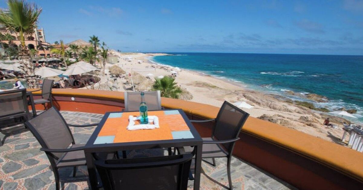 Terraza frente al mar con una mesa y sillas, con vista a la playa y al océano.