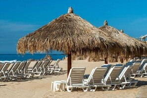 A beach with thatched umbrellas and sun loungers.