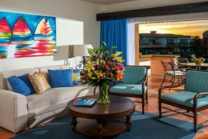 A hotel room with a sofa, a round wooden table, a vase of flowers, and a painting of sailboats.