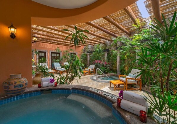 A pool area with lounge chairs, a hot tub, and tropical plants.