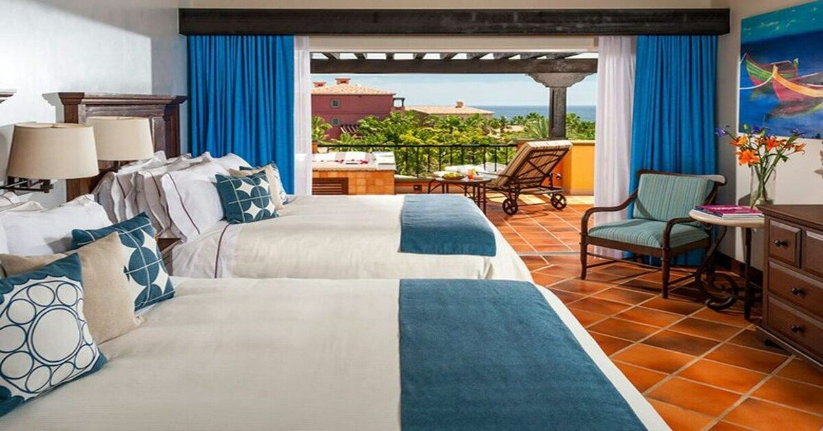 Habitación de hotel con dos camas, un balcón con vistas y un área de comedor.