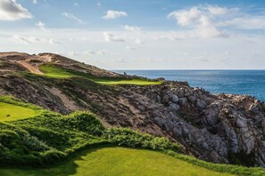 A coastal golf course with a rocky shoreline and a clear view of the ocean.