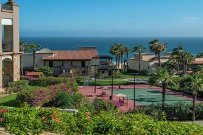 A resort with a tennis court, palm trees, and a view of the ocean.