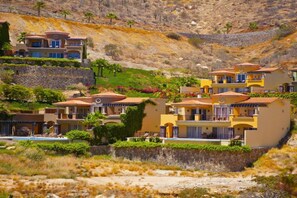 Un quartier résidentiel situé sur une colline, composé de plusieurs maisons à deux étages dotées de balcons, d’une piscine et bordé par une pente rocheuse.