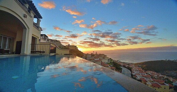 A swimming pool with a view of the sea and a sunset.