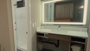 A bathroom with a white sink, a large mirror with under-cabinet lighting, a towel rack, and a door with a window. - New Star Inn. El Monte, CA - Los Angeles (El Monte)