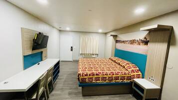 A compact hotel room with a bed, a desk, a chair, a TV, and a window with curtains.