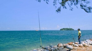 Un rivage rocheux parsemé de cannes à pêche, une personne en train de pêcher et une mer bleue et limpide.