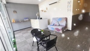Un hall d’hôtel moderne comprenant un comptoir d’accueil, un canapé et un espace repas avec une table et des chaises.