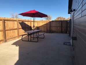 A patio area with a picnic table and a red umbrella.