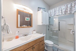 A bathroom with a white sink, wooden vanity, a glass shower enclosure, and a toilet.