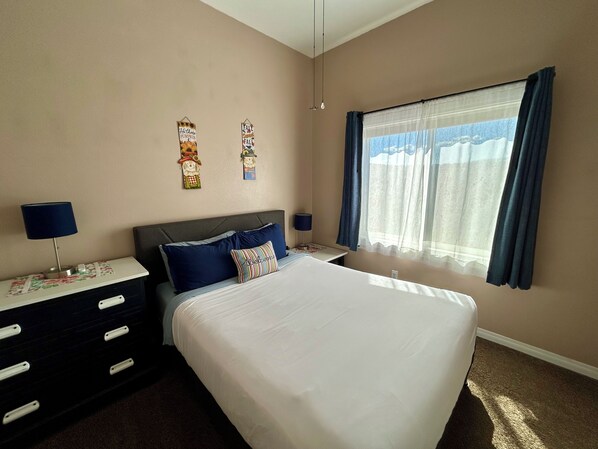 A bedroom with a large bed, two bedside tables, a dresser, and a window with curtains.