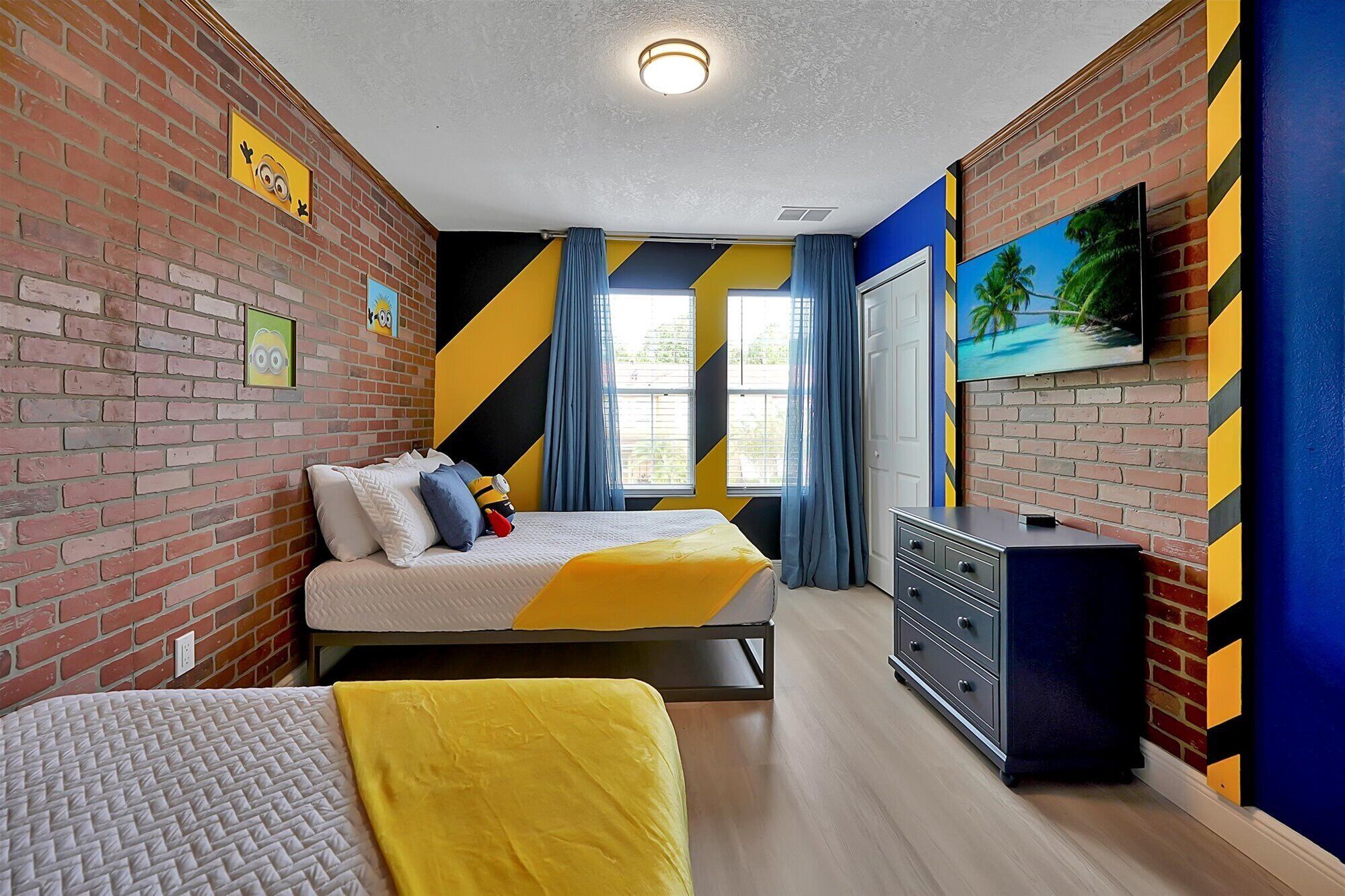 A hotel room with a brick wall, a bed with a yellow bedspread, a dresser, and a TV on the wall.