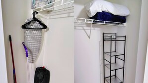 A room with a white wall, a metal shelf unit, a hanging rack, and a mop. - Cozy Studio with Kitchenette Attached (Davenport)