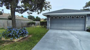 Eine Garage mit Wohngebiet, einer Betonauffahrt, einem Holzzaun und einem Baum mit blauen Blüten.