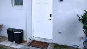 A white door with a window above it, a doorbell, and two black trash bins beside the door. - Cozy Studio with Kitchenette Attached (Davenport)