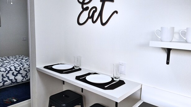 A compact kitchen with a white countertop, two stools, and a wall-mounted shelf with cups. - Cozy Studio with Kitchenette Attached (Davenport)
