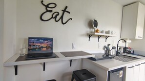 A modern kitchen with a laptop on a counter, a 'Eat' sign on the wall, and a coffee machine.