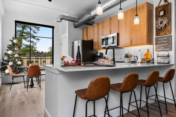 A modern kitchen with wooden cabinets, a central island with bar stools, a large window, and a Christmas tree. - Rock Nest by Vertical Design (Traverse City)