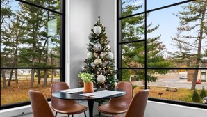 Une pièce d’angle avec une grande fenêtre, un sapin de Noël et une table entourée de quatre chaises.