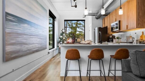 Une cuisine moderne avec des meubles en bois, un îlot central doté de tabourets de bar et un éclairage suspendu.