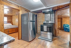Una cocina compacta con un refrigerador de acero inoxidable, horno y una pequeña zona de comedor con mantel a cuadros.