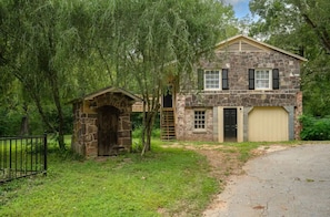 Una casa de piedra con garaje, una pequeña construcción de piedra y un patio cercado.