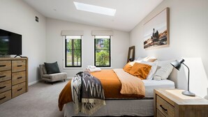 Un dormitorio con cama, una silla, televisor, escritorio y dos ventanas.